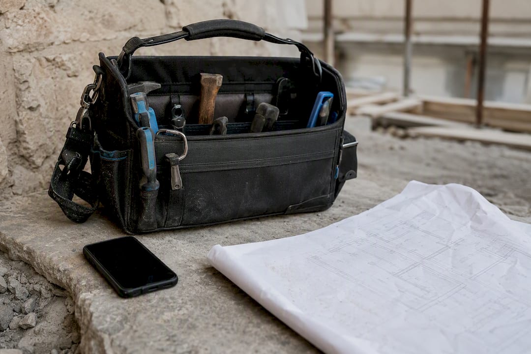 Werkzeugtasche, Smartphone und Bauplan liegen auf Holzbrettern